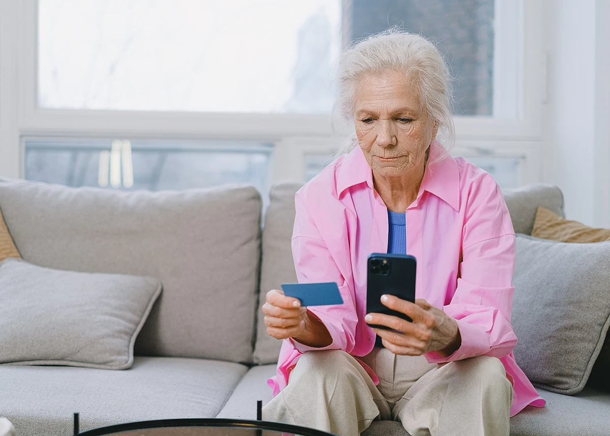 Alte Frau auf Sofa mit Handy in der Hand
